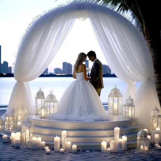 Wedding couple under a decorated arch with candles and lanterns by a waterfront.